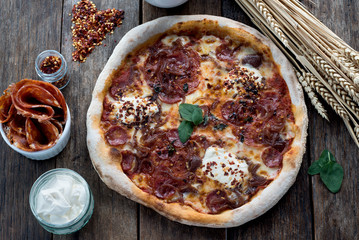 Basil leaves on an amazing fresh pizza is laying on a wooden table with all the ingredients around, with the heart shaped dried chilli rolled next to the pizza 