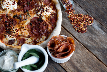 Close up of an amazing fresh pizza is laying on a wooden table with all the ingredients around, with the dried chilli rolled out as a heart form 