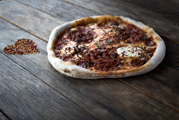 Only a heart shaped dried chilli and a pizza is laying on the nice old wooden table