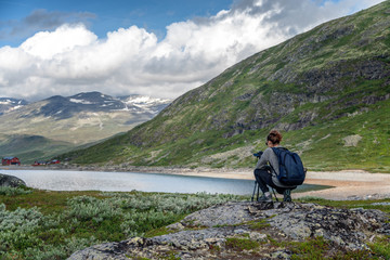 Fototapeta premium Young woman traveler professional photographer takes a picture of the landscape on the camera on a tripod, Norway, beautiful northern nature