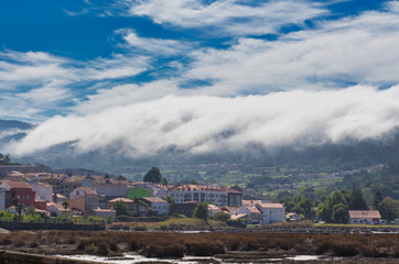 A sea of white clouds going down the mountains to the village of Noia in Galicia, Spain and reaching the sea ( low tide)