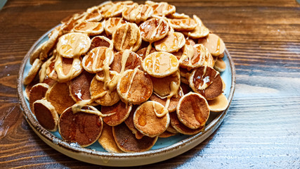 A plate of poffertjes with peanut butter and honey on the wooden background. Dutch mini pancakes ready for breakfast