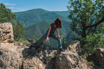 A full body shot of an unrecognizable young Caucasian female hiker standing on a rock doing a stretch in the French Alps mountains on a sunny summer day