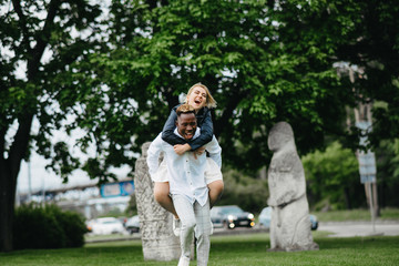 Fototapeta premium Interracial couple has fun and laughs in park on background of statues Polovtsian women.