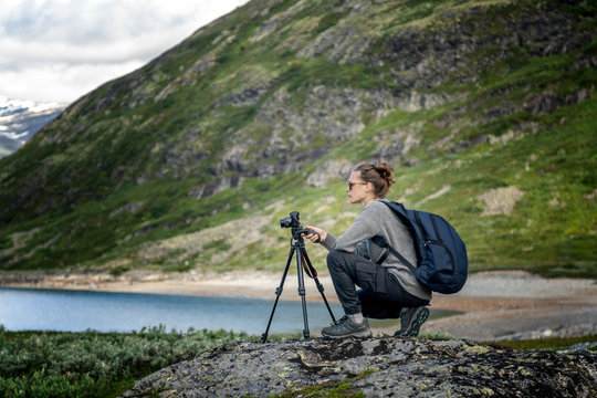 Young woman traveler professional photographer takes a picture of the landscape on the camera on a tripod, Norway, beautiful northern nature