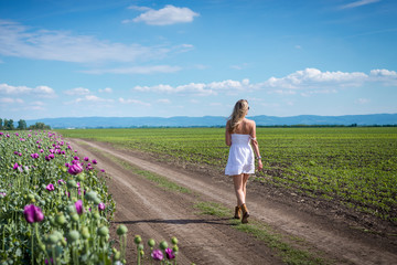 Adult caucasian woman in white dress walking through agricultural fields on sunny day with purple flowers and perfect blue sky