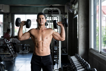 Fototapeta na wymiar Handsome man standing with beautiful muscular lifting dumbbells in the fitness gym. Man exercising in the sports center. Man taking care of his health dumbbells