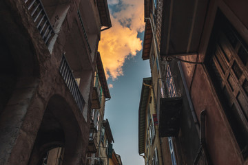 A picturesque low angle view of old tall apartment buildings in a French medieval village and blue sky with clouds illuminated by warm sunlight during sunset (Puget-Theniers, Alpes-Maritimes, France)