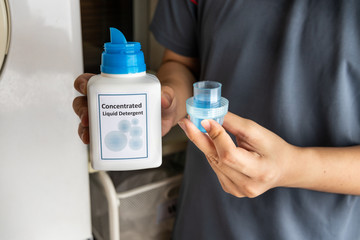 Person pouring concentrated liquid laundry detergent into measurement cap