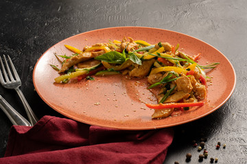 Chicken fillet with vegetables, pepper and onions. Plate with chicken on a black table.
