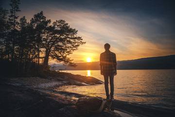Young woman stands with her back on the lake at sunset and looks at the sun