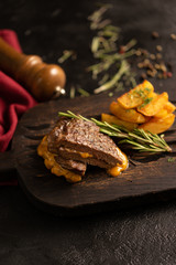 Hot grilled pork steak with rosemary, baked potatoes and cheese sauce. A hot dish of meat and potatoes on a dark cutting board. Blurred background.