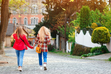 Obraz premium Two girlfriends holding hands and walking at street. Stylish trendy outfit, street style.