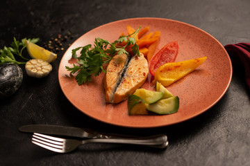 Steamed salmon fillet with fresh vegetables, pepper, zucchini, lemon and carrots with parsley. Hot seafood dish on a black table. Blurred background.