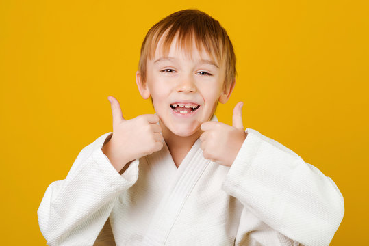 Face Portrait Of Happy Excited Boy. Child Wearing White Kimono. Sporty Kid On A Yellow Background. Martial Arts Concept.