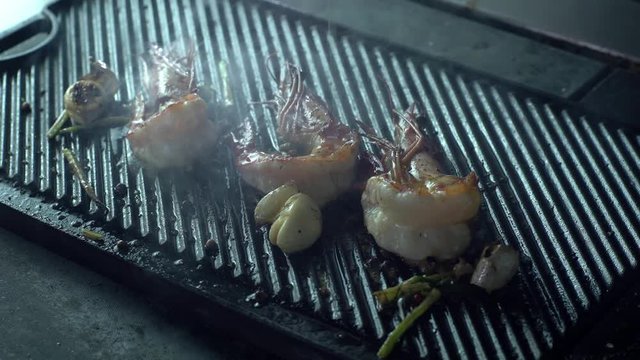 The chef sprinkles oil on the prawns that are grilled with herbs and garlic in thick smoke