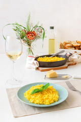 Risotto Milanese, wooden table with traditional Italian saffron risotto, glasses and pitcher of wine, bottle of olive oil, basket of bread and flowers, lunch for 2 people .