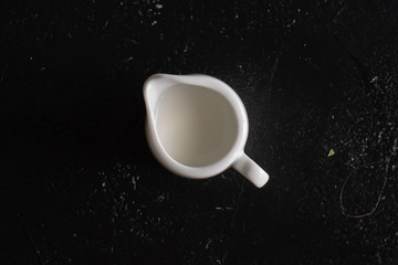 Creamer with cream on a black table. Jug of milk with milk on a black background.