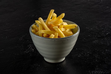 French fries in a deep ceramic cup on a black background.