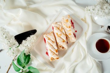 Fruit jam meringue cake garnished with hazelnut chips, among lilac flowers. Food photography. Advertising and commercial close up design.