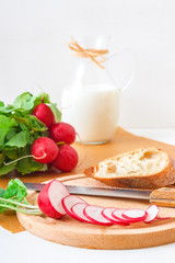 Italian twisted rosemary focaccia bread, ricotta cheese, fresh vegetable and herbs from a garden, radish, arugula, corn salad, sugar pea and milk, wooden mortar with red pepper. White wooden table. 