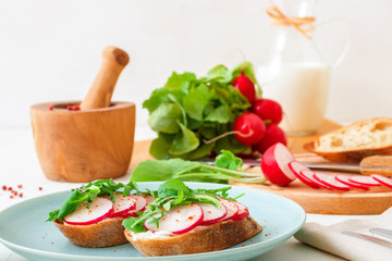 Italian twisted rosemary focaccia bread, ricotta cheese, fresh vegetable and herbs from a garden, radish, arugula, corn salad, sugar pea and milk, wooden mortar with red pepper. White wooden table. 
