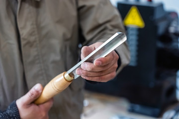 Man is holding the chisel for woodwork. Worker is keeping the new metal tool at workshop.