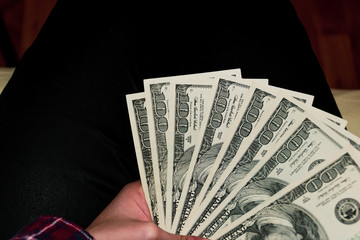 A close-up shot of an unrecognizable young Caucasian woman’s hand holding US dollars banknotes