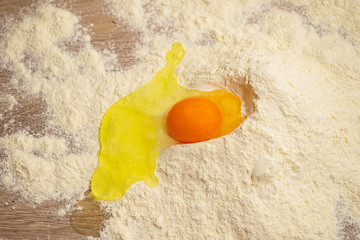 Broken egg in flour, on wood table
