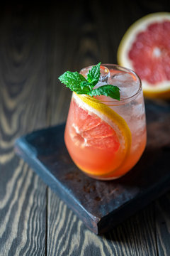 A glass of freshly squeezed grapefruit juice and mint on a dark wooden table. Refreshing summer cocktail.