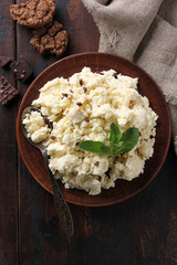 Fermented milk product. Cottage cheese  with chocolate and cookies in a clay plate on an old wooden background. Curd mass, fresh mint, spoon. Rustic. Flatlay, top view. Background image, copy space