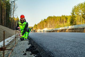 Surveyor engineer with equipment (theodolite or total positioning station) on the construction site of the road or building with construction machinery background