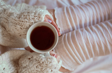 A girl in a white knitted sweater and knee socks holds a Cup of drink