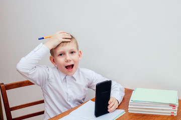 a boy of European appearance in a white shirt sits at a table and holds his head