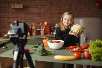 Little girl prepare the salad. Kid in the kitchen. Child with a vegetables. Girl shoot a blog.