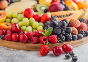 Fresh raw organic summer berries and exotic fruits in round large tray on light kitchen background. Papaya, grapes, nectarine, orange, raspberry, kiwi, strawberry, lychees, cherry and pineapple. Macro