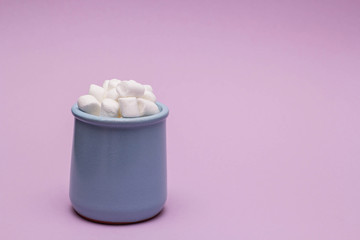 side view of a clay glass filled with white marshmallows on a lilac paper background