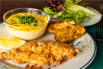 Fried fish with vegetables and piece of lemon on ceramic plate.