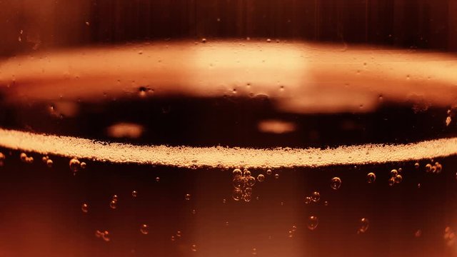Extreme close-up transparent glass full of fresh craft beer with rising up air bubbles slowmo. Macro shot cooled alcohol golden beverage with foam in bocal with water drops 4k