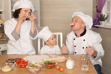 Mom, dad and son cook together from the dough. Teaching a child. Leisure quarantined family. Cheerful family in cook costumes cook pizza