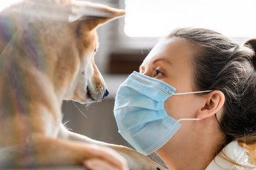 A girl in a medical mask and a dog of the Shiba Inu breed look yey to yey.  In difficult times of...