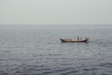Asian fishermen in a wooden boat sail in the middle of the sea. Copy, empty space for text