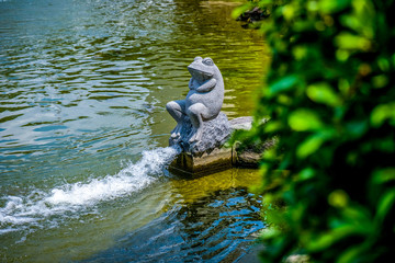 A sitting fog statue in the middle of a pond