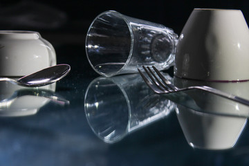 Crockeries items, Cup, glass, spoon, fork  on a table with reflection turned upside down