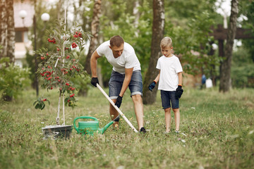 Family on a yard. Father with son planting a tree. Boy with a green funnel