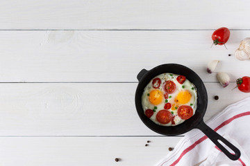 Fresh delicious breakfast of eggs and tomatoes with spices and red pepper, frying pan with fried eggs on white wooden background, top view, copy space