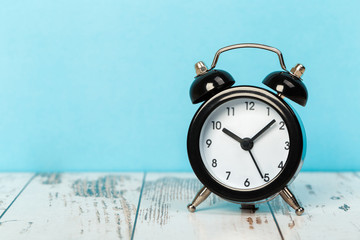 Black retro alarm clock with bells on a wooden table, daily routine concept.