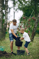 Family on a yard. Father with son planting a tree. Boy with a green funnel