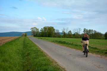 Obraz premium Young woman on a bike rides on a lonely country road in green nature