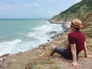Solo young man wearing casual clothes sitting on the cliff seeing beautiful ocean view Travel lifestyle and nature 